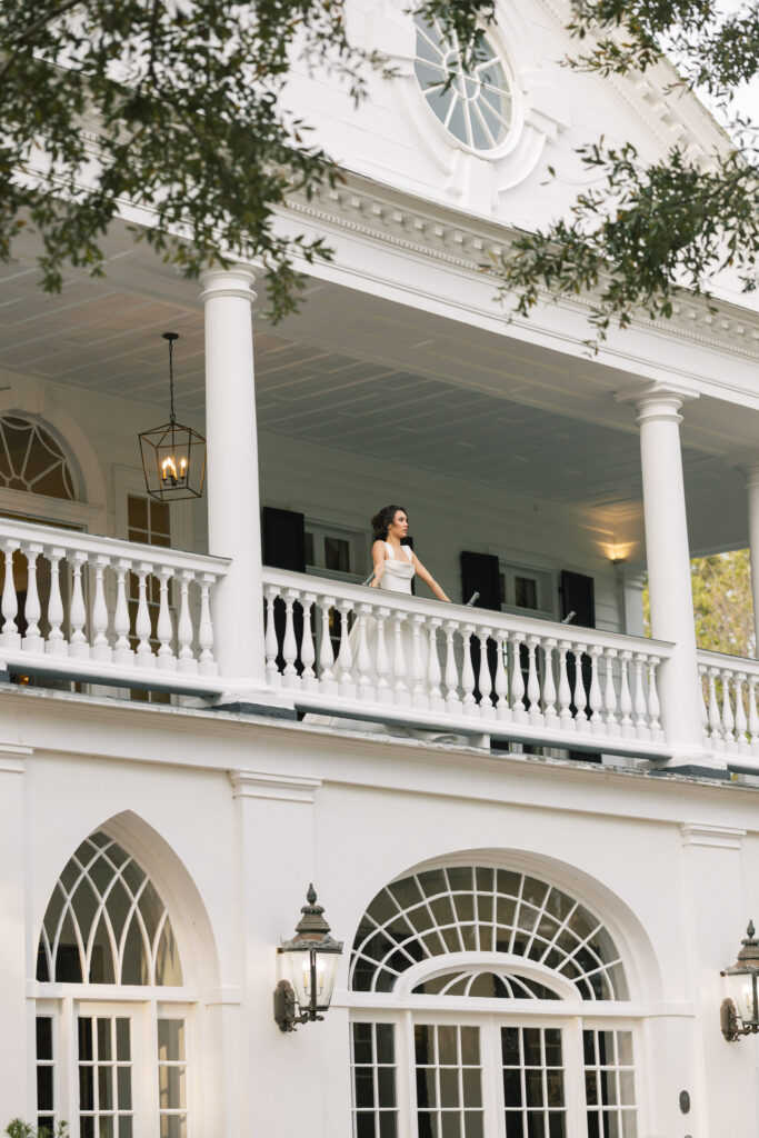 Bride standing on the balcony of a historic white mansion framed by columns and arched windows at one of the most refined historic wedding venues in Columbia SC.