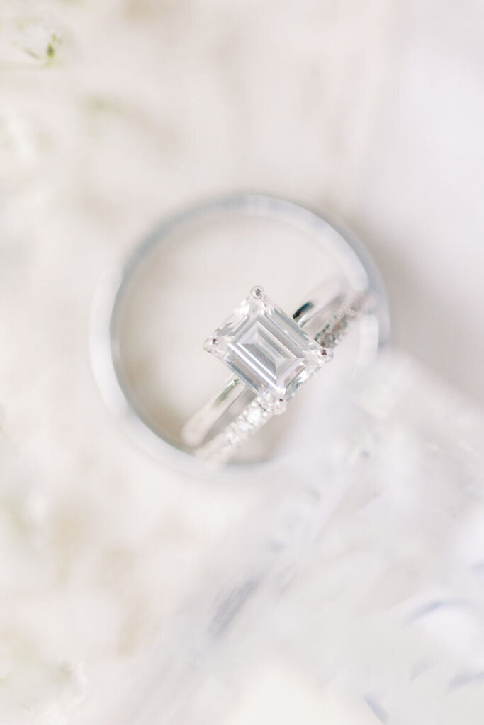 Close-up of an emerald-cut engagement ring resting in a silver dish with soft feathered texture, photographed by Charleston SC photographers.