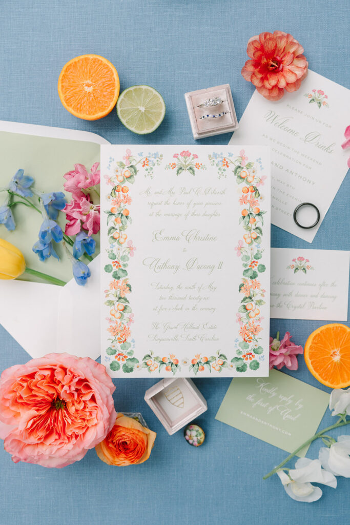 Invitation suite styled with citrus, blooms, and heirloom details on pale blue fabric, photographed as refined wedding details for a Greenville SC wedding photographer.