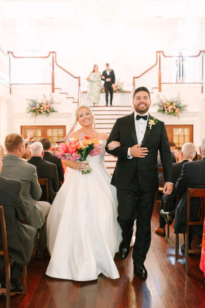 Bride and groom walk back down the aisle just after the ceremony with bright florals and happy guests around them, a beautiful just-married moment from a wedding in Greenville SC.