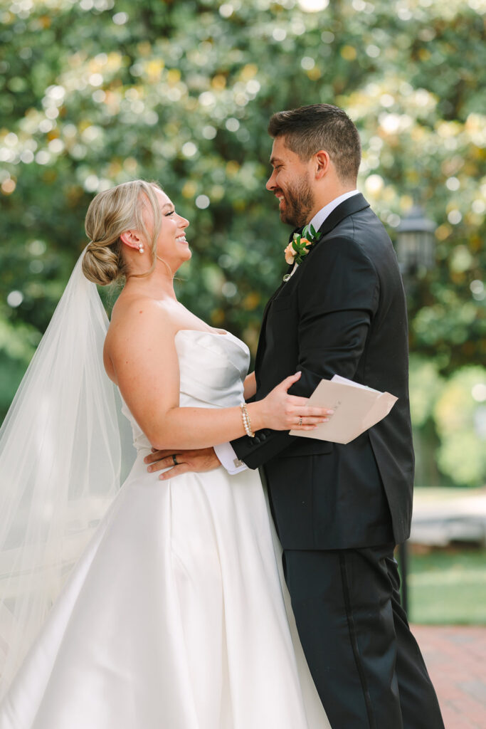 Bride and groom smile at each other in a quiet outdoor portrait surrounded by summer greenery, part of an intimate wedding in Greenville SC.
