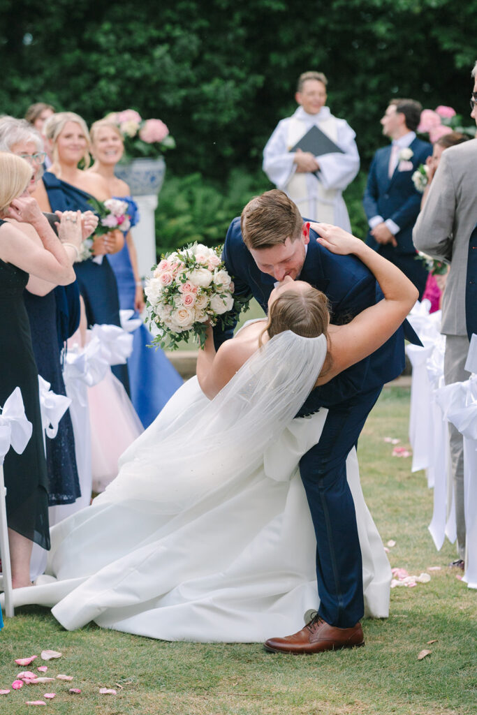 Newlyweds share a celebratory dip and kiss as their wedding party cheers behind them, capturing the joyful storytelling associated with a Charleston wedding photographer.