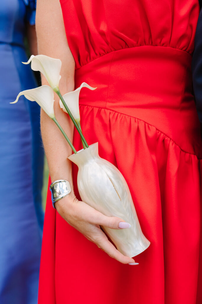 A bridesmaid in a vivid red dress carries white calla lilies in a sculptural vase, adding a bold editorial detail to this Botanical Gardens Clemson SC celebration.