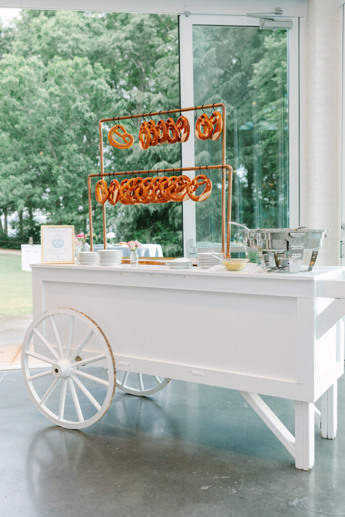 White dessert cart with an orange pretzel display inside a bright reception space, showing the personalized details captured by wedding photographers in Charleston, SC.