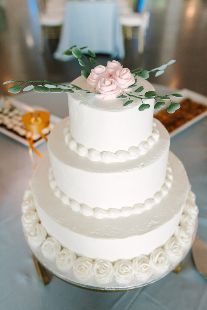 Three-tier white wedding cake decorated with delicate pink roses, greenery, and piped floral details, a refined reception touch at historic wedding venues in Charleston.