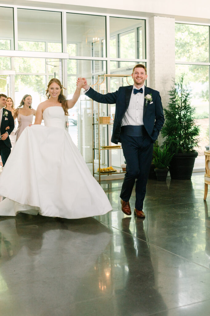 Newlyweds enter their reception hand in hand with guests behind them, capturing the celebratory atmosphere couples envision at the best Charleston wedding venues.