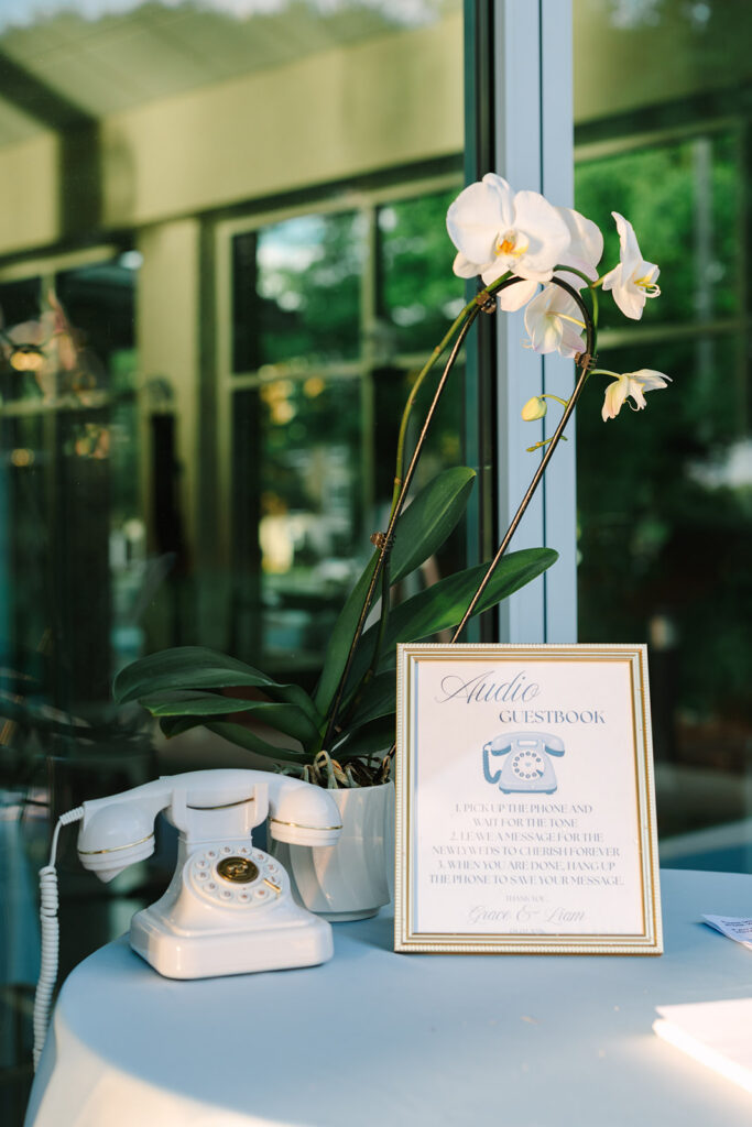 A vintage telephone, orchids, and framed audio guest book sign are styled on a reception table with thoughtful detail for wedding photography in Columbia SC.