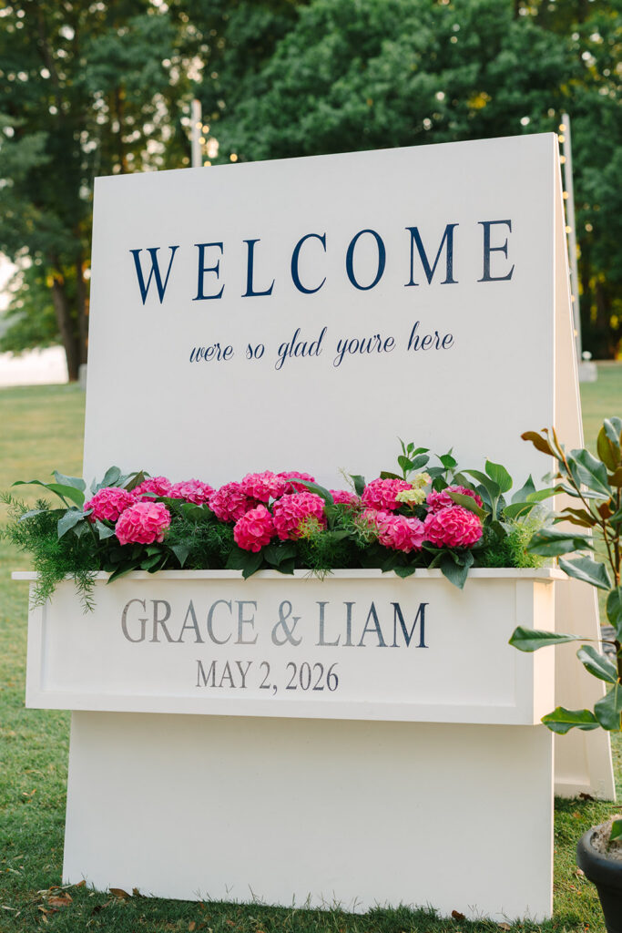 White wedding welcome sign for Grace and Liam framed with vibrant pink florals and greenery, a thoughtful detail often preserved through Charleston wedding photography.
