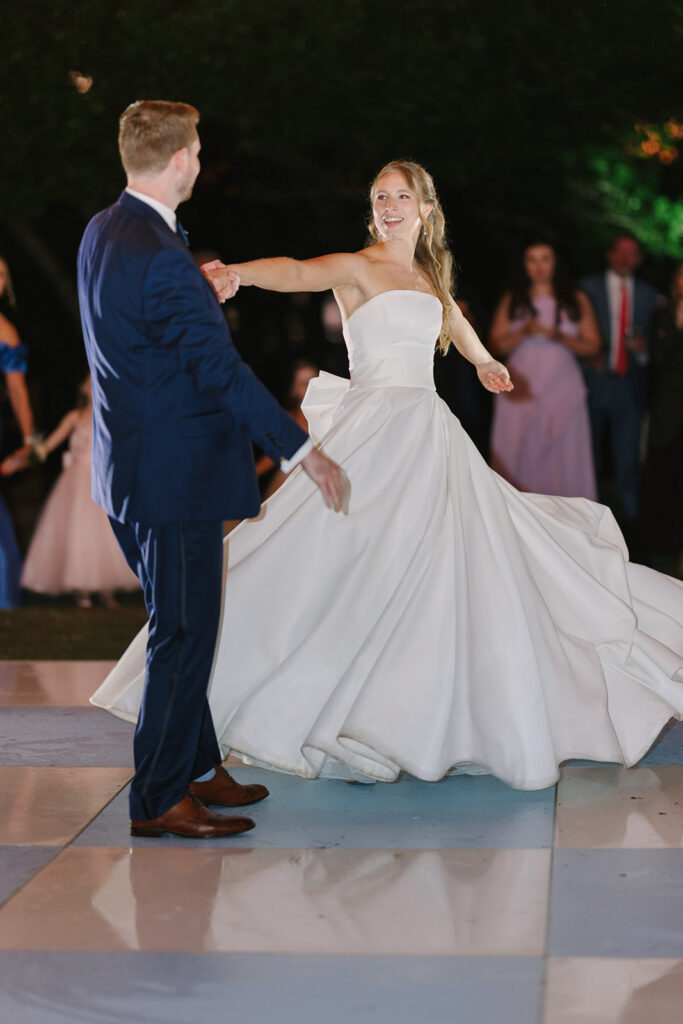 Bride and groom twirl together on the dance floor as guests watch in the background, capturing the joy of a real Clemson wedding reception.