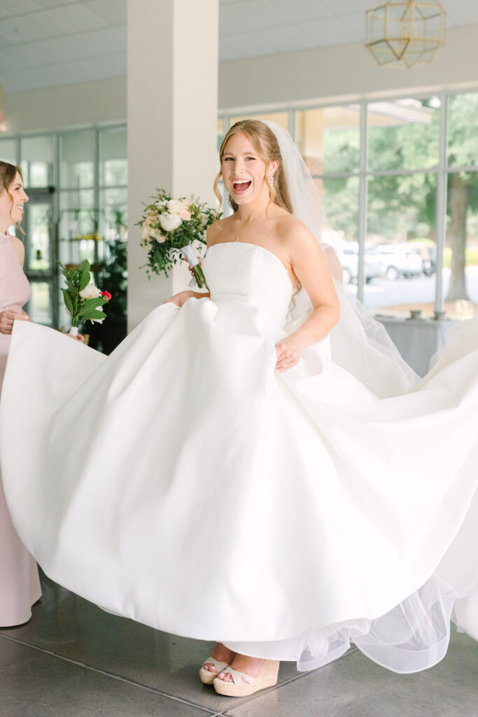 The bride lifts her gown with a joyful smile as she enters the reception space, a lively indoor moment photographed by Columbia SC photographers.