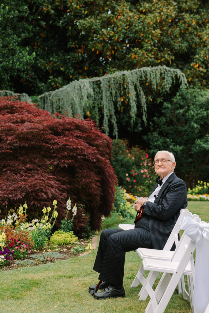 An older guest sits among lush gardens before the ceremony, adding a quiet documentary moment to an outdoor wedding venue in Columbia SC.