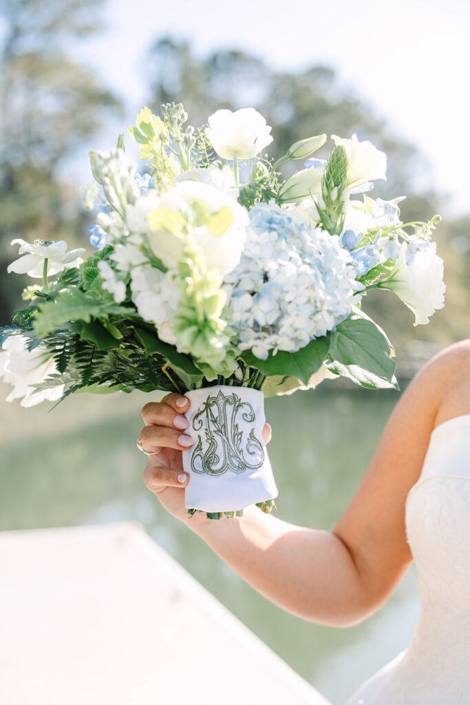 The bride holds her blue and white bouquet toward the camera in bright natural light, highlighting floral detail for a Columbia SC engagement and wedding photographer.
