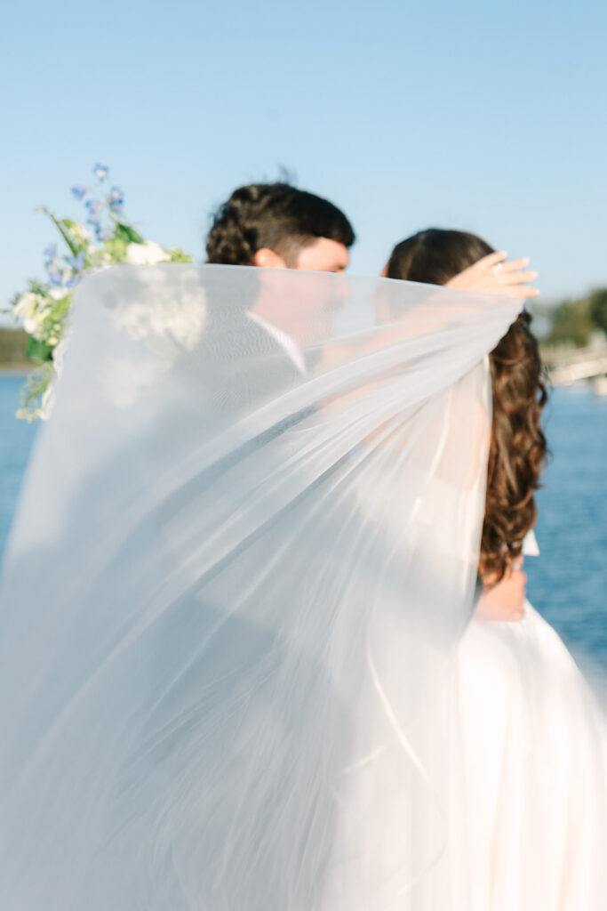 Newlyweds kiss outdoors as the bride’s sheer veil sweeps dramatically across the frame, creating a romantic, film-inspired portrait by a Charleston wedding photographer.