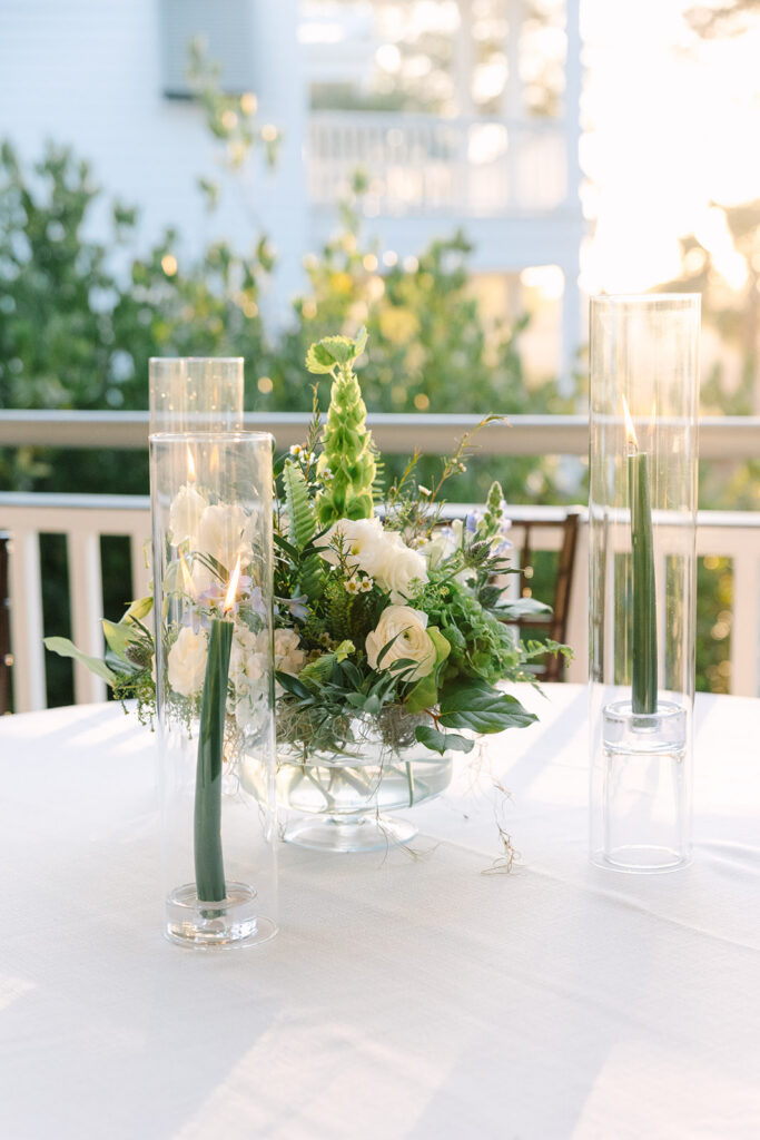 Elegant reception table with white linens, greenery, white florals, and tall glass candles glowing in soft evening light, a refined detail for Charleston wedding photos.