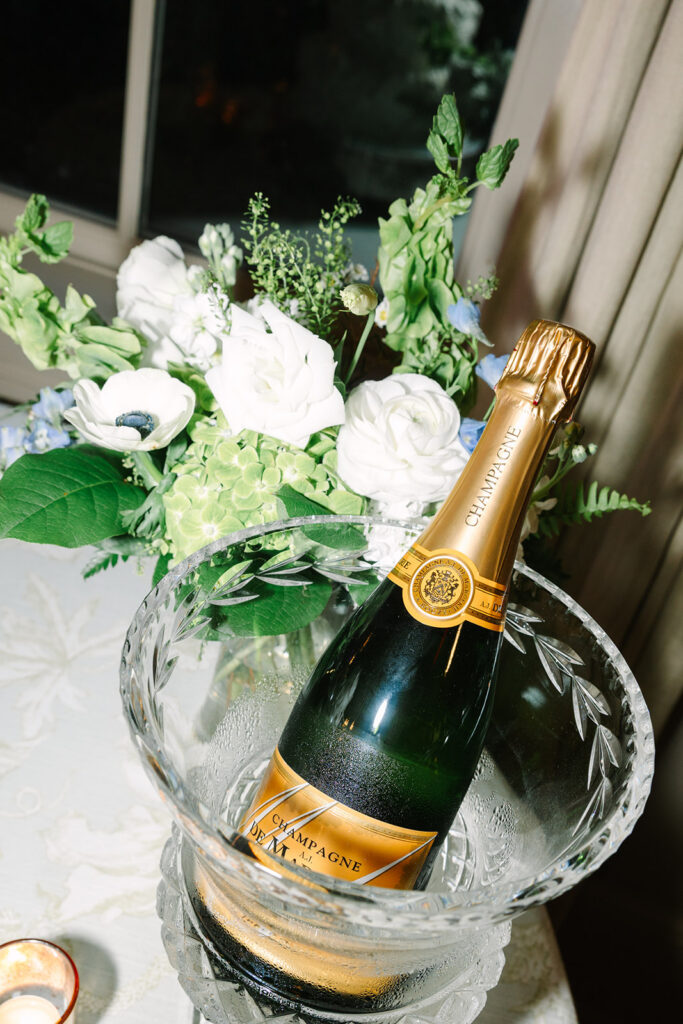 A champagne bottle rests in an ice bucket beside white florals and candlelight, styled as an elegant reception detail for photographers Columbia SC.