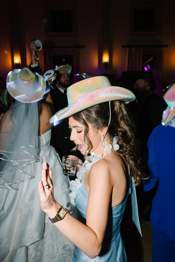 Wedding guest dances beneath colorful reception lights and playful cowboy hats, reflecting the unscripted celebration documented by Charleston SC wedding photographers.