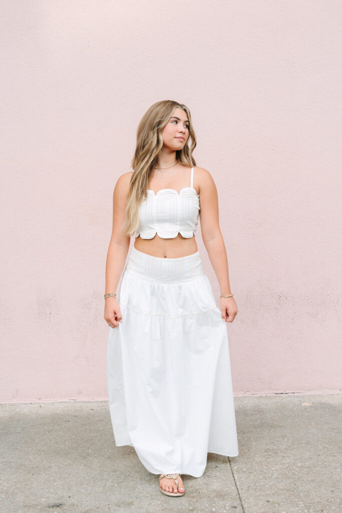 Colorful Charleston senior pictures at Mills Hotel. Pink wall with senior grad in white dress.