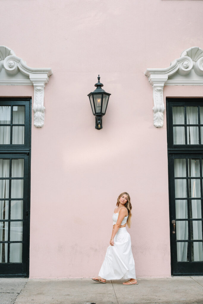 Colorful Charleston senior pictures at The Mills hotel. Senior walking in front of pink wall. Photographed by Stee Garman Photography.