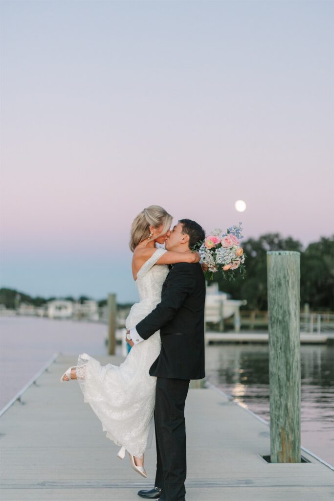 Groom lifting and kissing his bride on the waterfront dock at The Island House during evening portraits