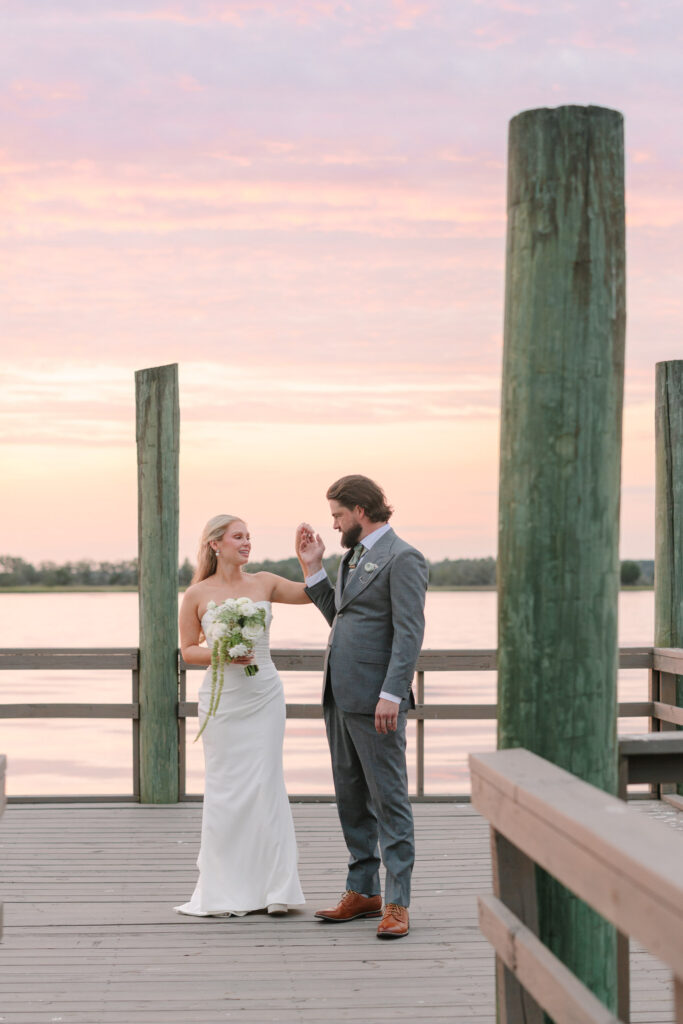 Savannah and Taylor smiling together on The Island House dock with pastel sunset skies over the water