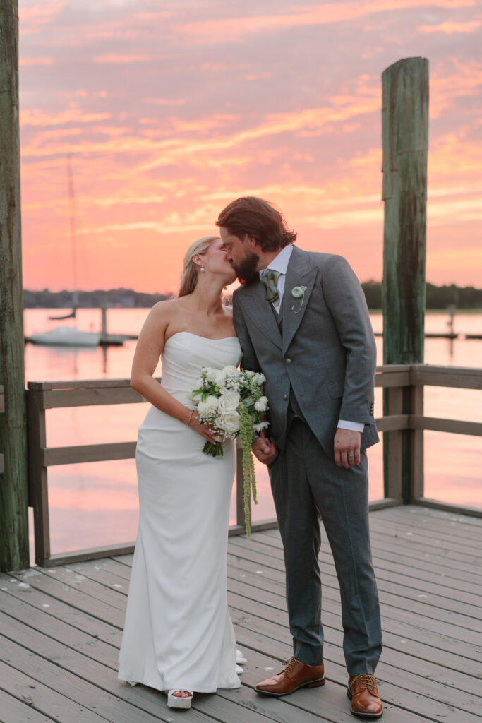 Savannah and Taylor kissing on the dock beneath a pink sunset at The Island House on Johns Island
