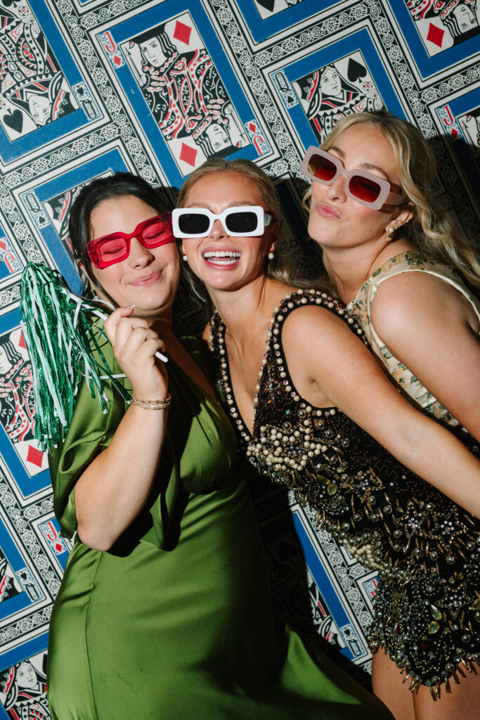 Three women wearing colorful sunglasses and posing in a photo booth at The Island House