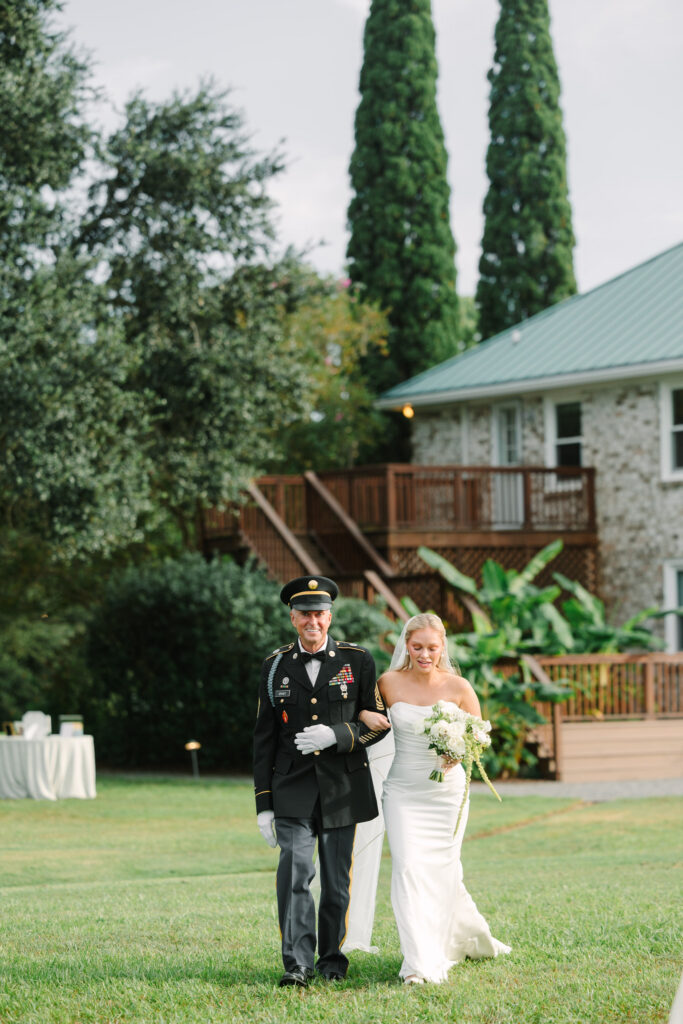 Bride walking across the lawn with her escort at The Island House wedding venue